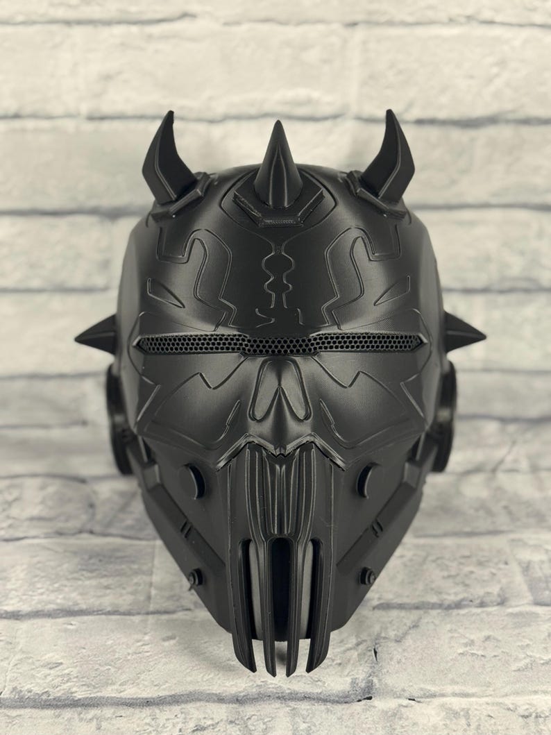 Op de afbeelding: Een zwart, ingewikkeld ontworpen helm met een dreigende uitstraling. De helm heeft meerdere spikes en hoorns, een mesh oogbedekking en een gedetailleerd frontpaneel. Het ontwerp suggereert een futuristisch of fantasiethema.