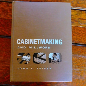 Può includere: Un libro marrone con il titolo "Cabinetmaking and Millwork" di John L. Feier. La copertina presenta illustrazioni di strumenti per la lavorazione del legno e una persona che lavora su un armadio.