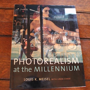 May include: A hardcover book titled "Photorealism at the Millennium" by Louis K. Meisel with Linda Chase. The cover features a photo of a woman and a city scene with the word "ALEXANDER" visible.