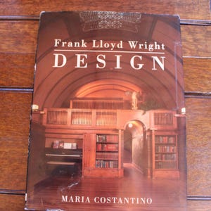 Könnte beinhalten: Buchcover mit einem Foto eines Holzinnenraums mit gewölbter Decke, Bücherregalen und einem Klavier. Der Titel des Buches lautet "Frank Lloyd Wright DESIGN" und der Autor ist "MARIA COSTANTINO".