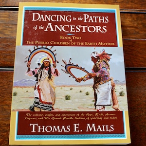 May include: A hardcover book titled "Dancing in the Paths of the Ancestors" by Thomas E. Mails. The cover features an illustration of Native American figures in traditional attire, with text describing the book's focus on Pueblo culture, crafts, and ceremonies.