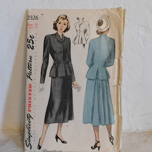 May include: A vintage Simplicity sewing pattern, size 14, with illustrations of a two-piece suit and a dress. The pattern shows a dark-coloured jacket and skirt, and a light blue dress. The price is 25c.