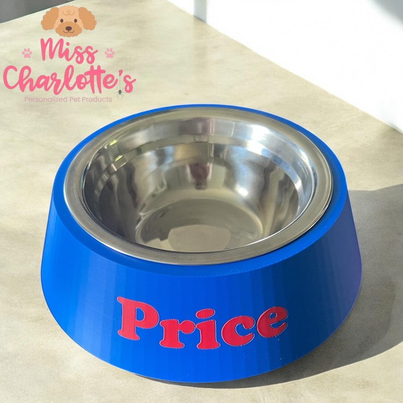 A bright blue dog bowl with a stainless steel insert has the name "Price" in red letters on the front, sitting on a light-colored surface.