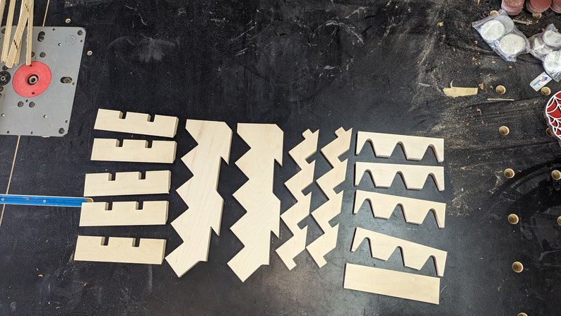 May include: A set of wooden pieces for a craft project. The pieces are cut in different shapes, including zigzags, waves, and rectangles. The pieces are made of light-colored wood and are arranged on a dark surface.