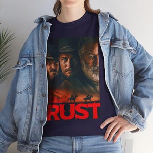 Könnte beinhalten: Ein marineblaues T-Shirt mit einem Aufdruck von drei Männern in Cowboyhüten und dem Wort "RUST" in roten Buchstaben.