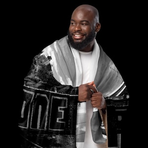 May include: A black and white scarf with a cityscape design and the word "ONE" printed on it. The scarf is draped over a person's shoulders, with the design visible. The scarf appears to be made of a soft material.