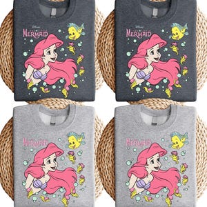 Retro-style Disney Little Mermaid shirt featuring Princess Ariel, perfect for girls’ trips, family vacations, or matching outfits at Walt Disney World. This playful tee or hoodie showcases nostalgic design elements with seashells, waves, and classic Ariel artwork. Great for park days, Disney cruise wear, or fans of the original Disney princess with a love for under-the-sea adventure and magical memories.