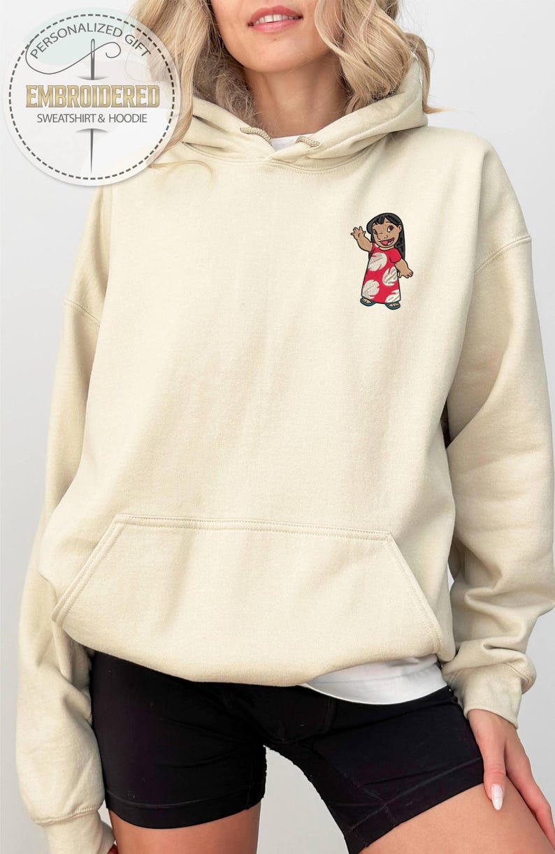 Puede incluir: Sudadera con capucha bordada de color crema con bolsillo delantero y capucha con cord&oacute;n. El dise&ntilde;o presenta un personaje de dibujos animados con un vestido rojo con lunares blancos. El texto "PERSONALIZED GIFT EMBROIDERED SWEATSHIRT & HOODIE" est&aacute; impreso arriba a la izquierda.