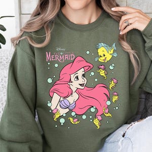 Retro-style Disney Little Mermaid shirt featuring Princess Ariel, perfect for girls’ trips, family vacations, or matching outfits at Walt Disney World. This playful tee or hoodie showcases nostalgic design elements with seashells, waves, and classic Ariel artwork. Great for park days, Disney cruise wear, or fans of the original Disney princess with a love for under-the-sea adventure and magical memories.