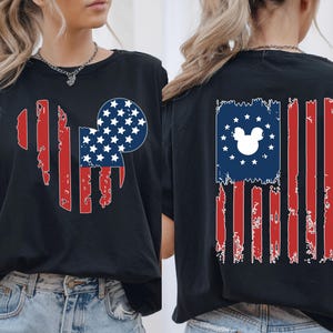 May include: Black t-shirt with a distressed American flag design incorporating a Mickey Mouse silhouette. The front features a Mickey head shape with red stripes and a blue circle with white stars. The back has a similar flag design.