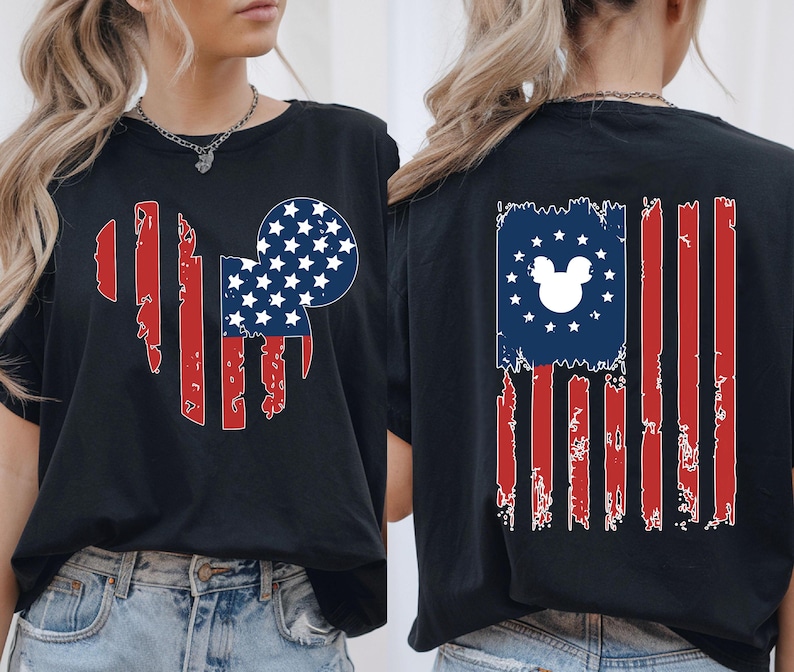 May include: Black t-shirt with a distressed American flag design incorporating a Mickey Mouse silhouette. The front features a Mickey head shape with red stripes and a blue circle with white stars. The back has a similar flag design.
