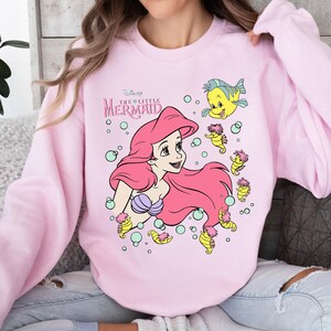 Retro-style Disney Little Mermaid shirt featuring Princess Ariel, perfect for girls’ trips, family vacations, or matching outfits at Walt Disney World. This playful tee or hoodie showcases nostalgic design elements with seashells, waves, and classic Ariel artwork. Great for park days, Disney cruise wear, or fans of the original Disney princess with a love for under-the-sea adventure and magical memories.