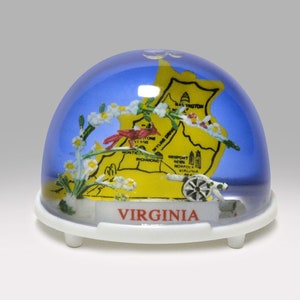 May include: A snow globe featuring a map of Virginia with a yellow background and blue dome. The globe includes a red cardinal, white flowers, and a miniature cannon. The base is white with the word "VIRGINIA" in red.