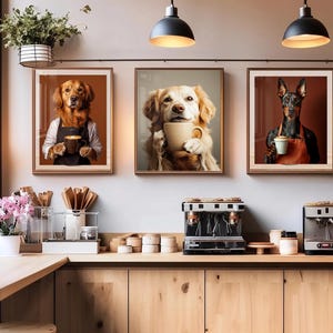 May include: Three framed dog portraits hang on a wall above a coffee bar. Each dog is holding a coffee cup. The first is a golden retriever wearing an apron. The second is a golden retriever holding a cup. The third is a Doberman wearing an apron.