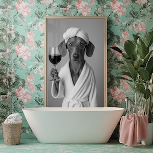 Op de afbeelding: Zwart-witfoto van een hond die een witte badjas draagt en een glas wijn vasthoudt. De hond bevindt zich in een badkamer met een wit bad en een groene bloemenbehang.
