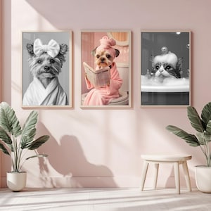 Op de afbeelding: Drie ingelijste zwart-witfoto's van huisdieren die verwend worden. De eerste foto toont een Yorkshire Terrier die een witte badjas en een strik draagt. De tweede foto toont een Yorkshire Terrier die een roze badjas draagt en een krant leest. De derde foto toont een kat die een witte badjas draagt en een bad neemt.