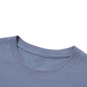 Peut inclure: Gros plan d'un t-shirt bleu &agrave; col rond. Le col est c&ocirc;tel&eacute; et le tissu semble &ecirc;tre un m&eacute;lange de coton doux. Le t-shirt est de couleur unie sans graphiques ni motifs visibles.