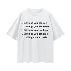 May include: White t-shirt with short sleeves. The shirt features the text: "5 things you can see, 4 things you can touch, 3 things you can hear, 2 things you can smell, 1 thing you can taste."