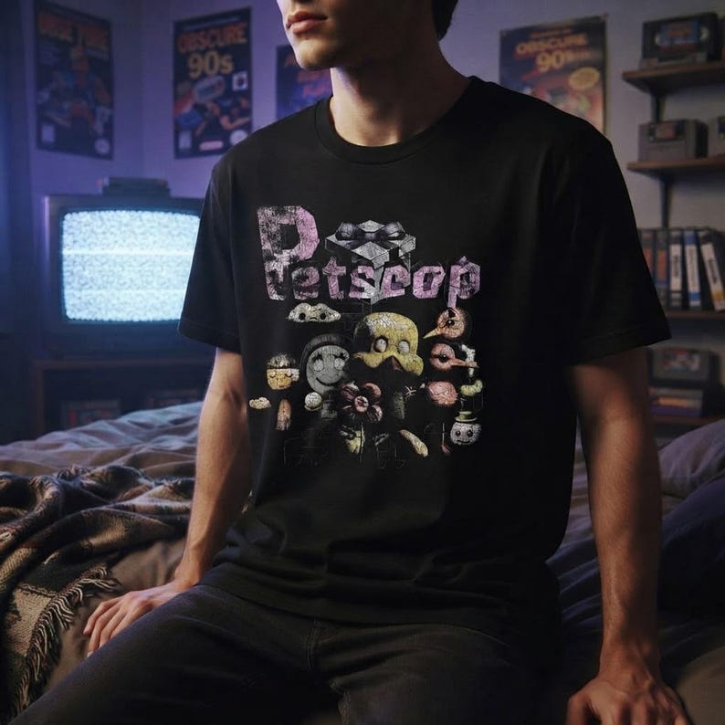 A person wearing the black Petscop graphic t-shirt in a dimly lit retro gaming bedroom.