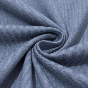 Close-up of folded blue-grey cotton fabric showing the soft knit texture and swirled folds.