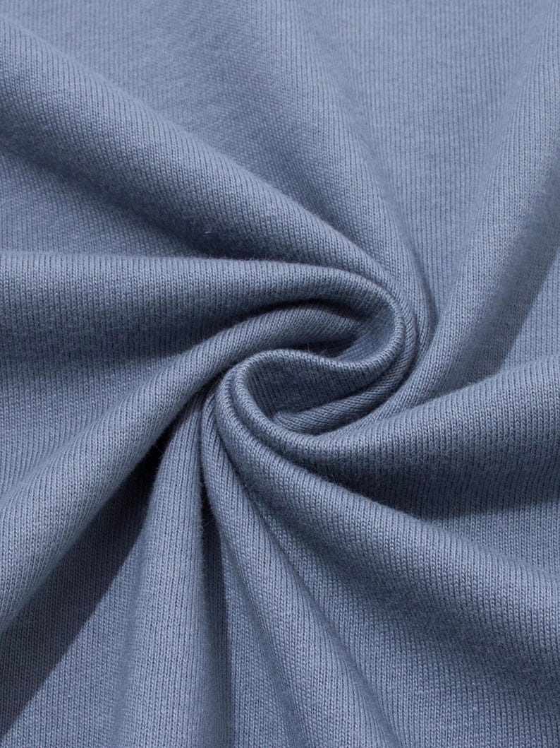 Close-up of folded blue-grey cotton fabric showing the soft knit texture and swirled folds.