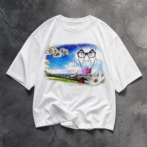 Puede incluir: Camiseta blanca con una ilustración de dibujos animados. El gráfico representa a un hombre con gafas haciendo un gesto obsceno, sobre un fondo de flores, cielo y nubes. El diseño es una declaración humorística y audaz.