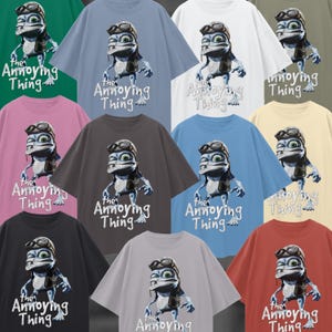 May include: A collection of oversized t-shirts in various colors, each featuring a cartoon frog character wearing goggles and a leather jacket. The text "the Annoying Thing" is printed below the frog.