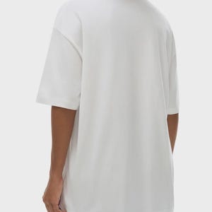 May include: A white, short-sleeved t-shirt with a relaxed fit. The shirt has a crew neck and a simple, minimalist design. The fabric appears to be a soft, lightweight material, suitable for casual wear.