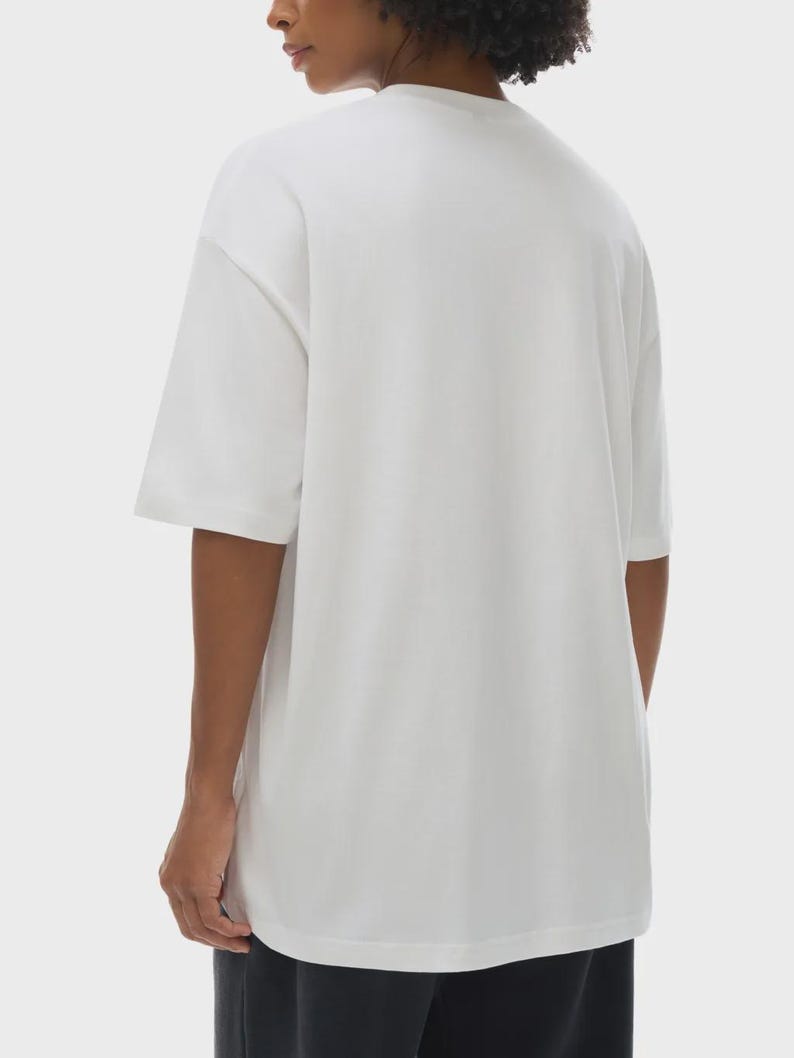May include: A white, short-sleeved t-shirt with a relaxed fit. The shirt has a crew neck and a simple, minimalist design. The fabric appears to be a soft, lightweight material, suitable for casual wear.