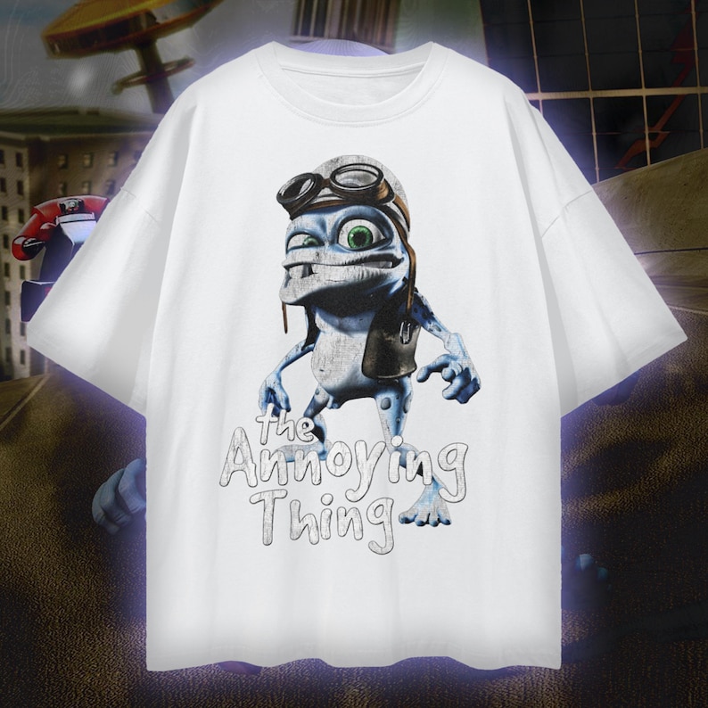 May include: White t-shirt featuring a cartoon character with goggles and a leather jacket. The character is blue and gray with green eyes. The text "The Annoying Thing" is printed below the character in a handwritten style.