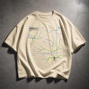 Puede incluir: Camiseta color crema con diseño de mapa en azul y verde. La camiseta presenta el texto "AMBIENT 1 MUSIC FOR AIRPORTS" en negro. Cuello redondo, mangas cortas, ideal para uso casual.