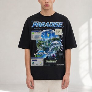 May include: Black t-shirt with a graphic design featuring the word "PARADISE" in blue and white, a dolphin, and a Windows-themed graphic. The shirt also includes the text "welcome to" and "loading a better tomorrow."