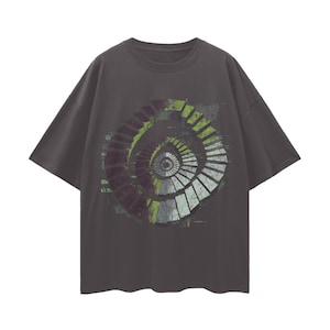 Puede incluir: Camiseta gris oscuro con un diseño de escalera de caracol en tonos verdes, blancos y morados. El gráfico está centrado en la parte delantera de la camiseta. La camiseta tiene mangas cortas y cuello redondo.