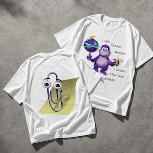 Op de afbeelding: Twee witte T-shirts met cartoonafbeeldingen. Eén shirt heeft een paarse aap met een wereldbol en banaan, met de tekst: "I Talk! I E-Mail! I Browse! I Laugh! I Tell Facts! Schedule!". Het andere shirt heeft een cartoon paperclip op een geel notitieblok.