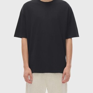 May include: A black, short-sleeved t-shirt with a crew neck. The shirt is paired with light beige shorts. The model is standing in front of a plain, light background. The t-shirt appears to be made of a soft, comfortable material.