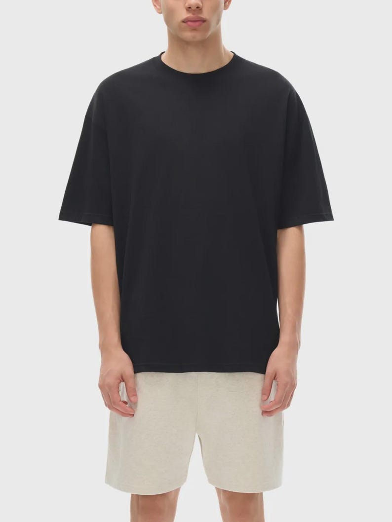 May include: A black, short-sleeved t-shirt with a crew neck. The shirt is paired with light beige shorts. The model is standing in front of a plain, light background. The t-shirt appears to be made of a soft, comfortable material.