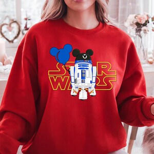 Star Wars shirt featuring fan-favorite characters like Darth Vader, Baby Yoda, Chewbacca, and Han Solo with fun Mickey head accents. This soft, unisex tee or sweatshirt is perfect for Disney trips, Star Wars Day, or matching family outfits. A playful mix of galaxy and Disney magic, ideal for park hopping, themed parties, or gifting to fans of the Mandalorian and the whole Star Wars crew.