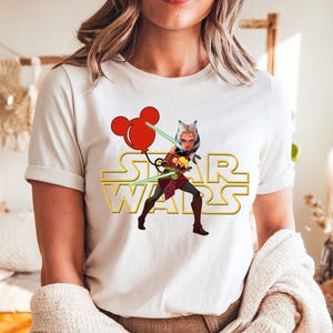 Star Wars shirt featuring fan-favorite characters like Darth Vader, Baby Yoda, Chewbacca, and Han Solo with fun Mickey head accents. This soft, unisex tee or sweatshirt is perfect for Disney trips, Star Wars Day, or matching family outfits. A playful mix of galaxy and Disney magic, ideal for park hopping, themed parties, or gifting to fans of the Mandalorian and the whole Star Wars crew.