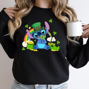 May include: Black sweatshirt featuring a cartoon character dressed for St. Patrick's Day. The character wears a green hat, glasses, and holds a shamrock. A rainbow, pot of gold, and green shamrocks are also visible.