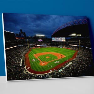 May include: A night view of a baseball stadium with a green field and a brown dirt infield. The stadium is lit up with lights and there are people in the stands. The stadium has a retractable roof that is open.