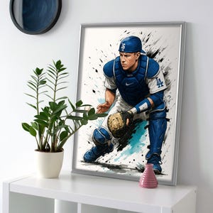 May include: Framed art print of a baseball catcher in a blue and white uniform, with the number 16 on the cap. The artwork features a watercolor style with black and teal paint splatters. The catcher is in a crouched position, ready to catch the ball.