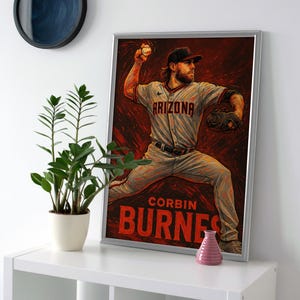 May include: Framed artwork featuring a baseball player in action, wearing an Arizona jersey. The artwork has a red and brown background with the name "CORBIN BURNES" in large letters. The image is in a silver frame.