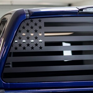 May include: A blue pickup truck with a black American flag decal on the rear window.