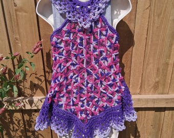 Op de afbeelding: Een handgemaakte gehaakte top in tinten paars, roze en wit. De top heeft een halterhalslijn en een geschulpte zoom. Het openwerkontwerp creëert een delicate en luchtige uitstraling, perfect voor warm weer.