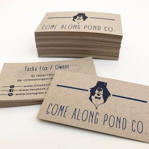 May include: A stack of brown kraft paper business cards with the text "COME ALONG POND CO." and a black and white illustration of a dog wearing a top hat and bow tie. The contact information for Tasha Fox, Owner, is listed on the card, including a phone number, email address, and links to social media.