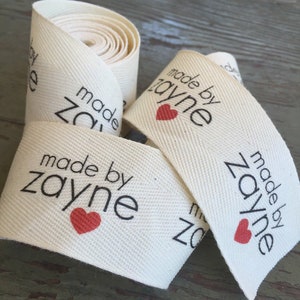 Op de afbeelding: Een rol witte katoenen stof met een zwart en rood label met de tekst "made by zayne" met een rood hart.