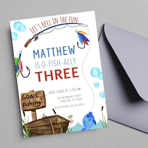 Puede incluir: Una invitación con temática de pesca, con ilustraciones en acuarela. El texto incluye "Let's Reel in the Fun", "Matthew is O-Fish-ally Three" y detalles del evento. El diseño presenta una caña de pescar, flotadores, un barco y un pez azul sonriente.