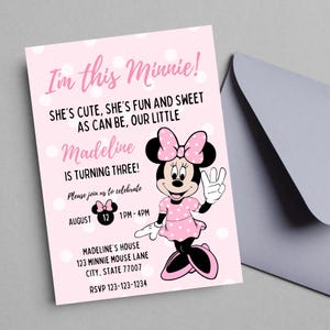 以下が含まれることがあります： 白い水玉模様のピンク色のミニーマウスの誕生日パーティーの招待状。「I'm this Minnie!」と書かれており、「Madeline is turning three!」とパーティーの詳細が記載されています。灰色の封筒が背景にあります。