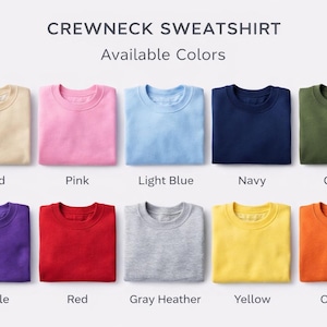 K&ouml;nnte beinhalten: Gefaltete Crewneck-Sweatshirts in verschiedenen Farben: Sand, Pink, Hellblau, Marine, Olive, Lila, Rot, Grau meliert, Gelb und Orange. Der Text "CREWNECK SWEATSHIRT Available Colors" steht oben.