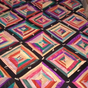 May include: A colorful quilt with a geometric diamond pattern. The quilt features a variety of colors including pink, purple, green, and black. The quilt is on a bed with a gray headboard.